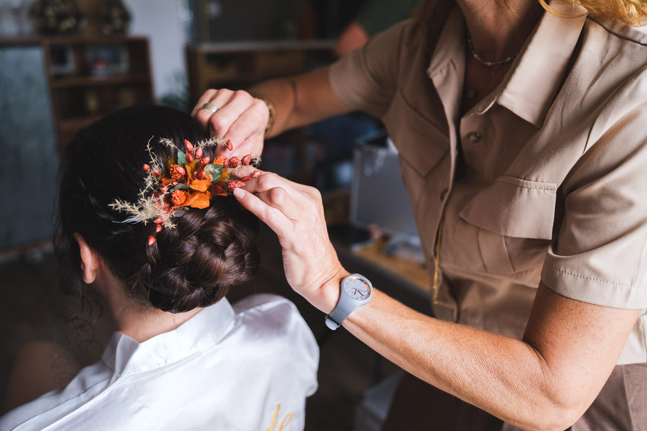 Une pièce florale séchée aux tons orangés fixée dans le chignon tressé de la mariée.