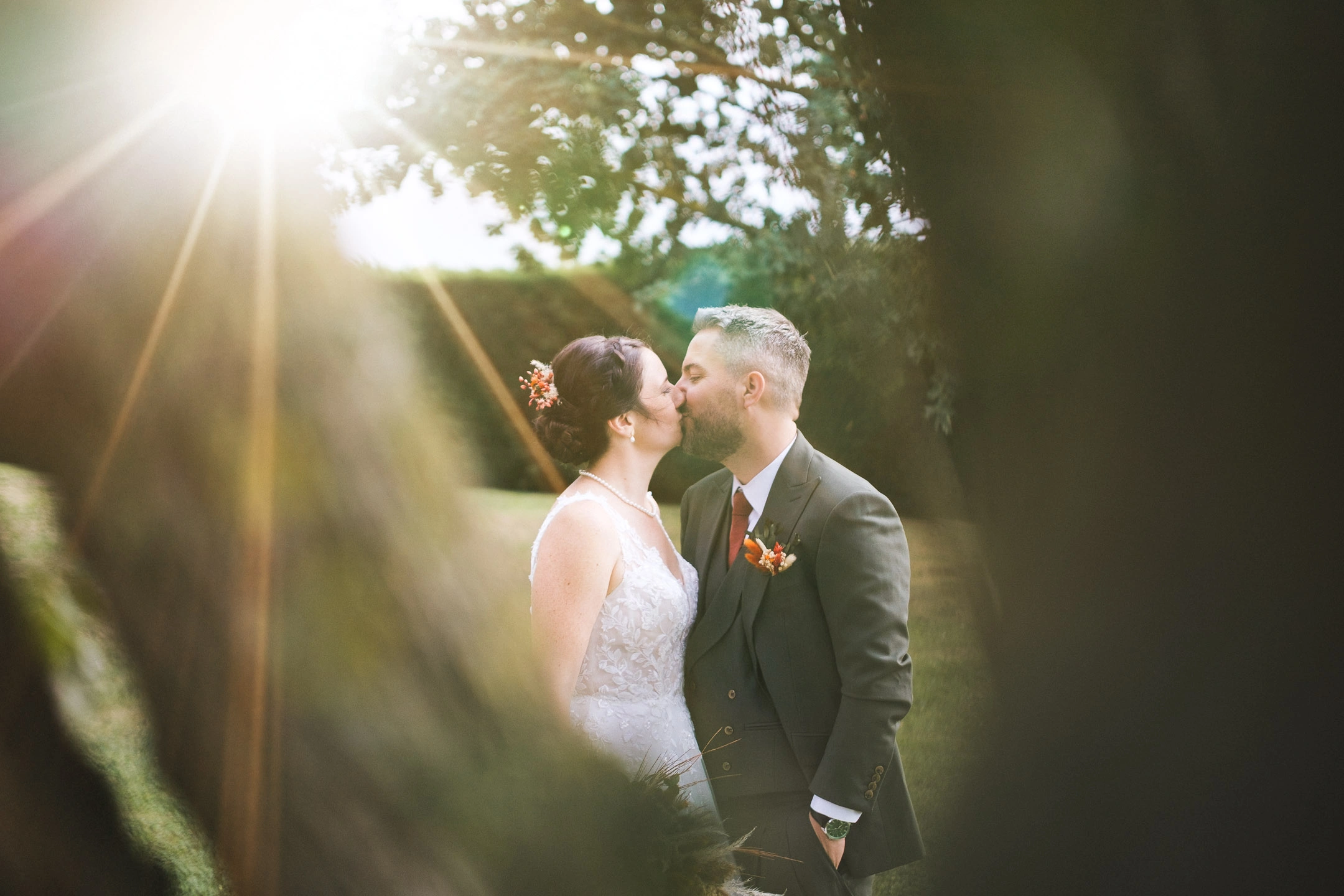 Camille et Florian s'embrassant dans un jardin, éclairés à contre-jour par un soleil rayonnant.