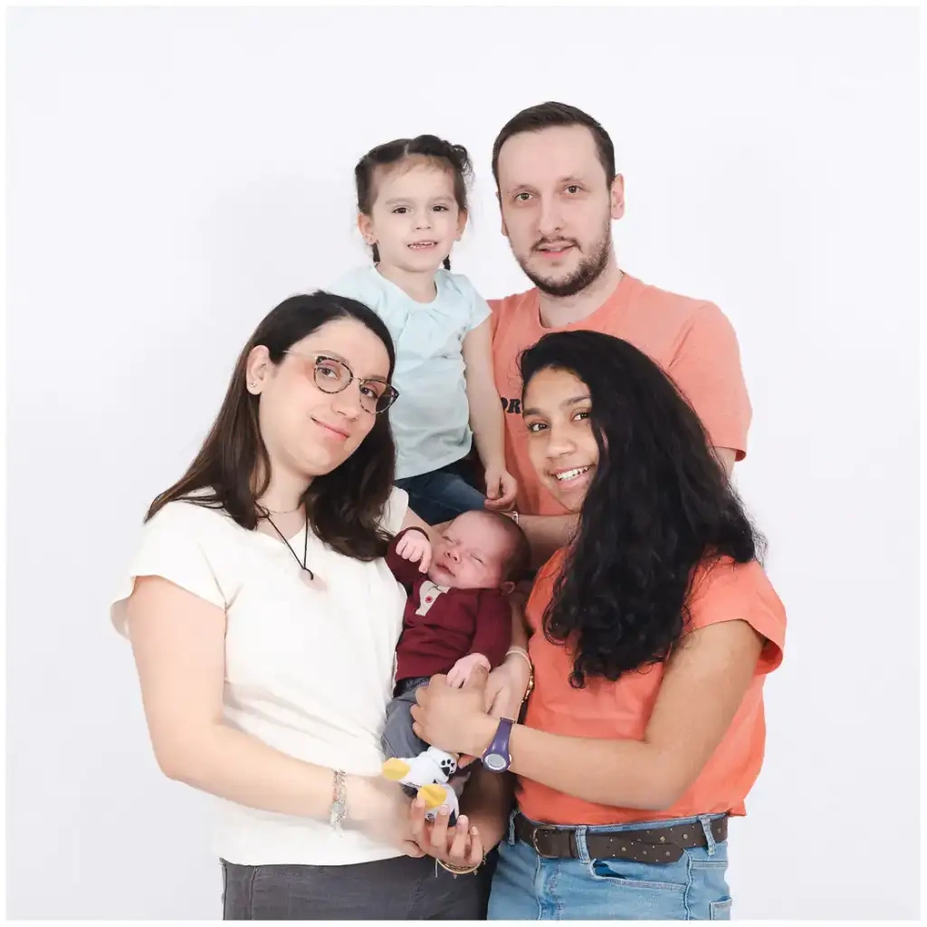 Une famille de cinq personnes entoure un nouveau-né endormi devant un fond blanc.