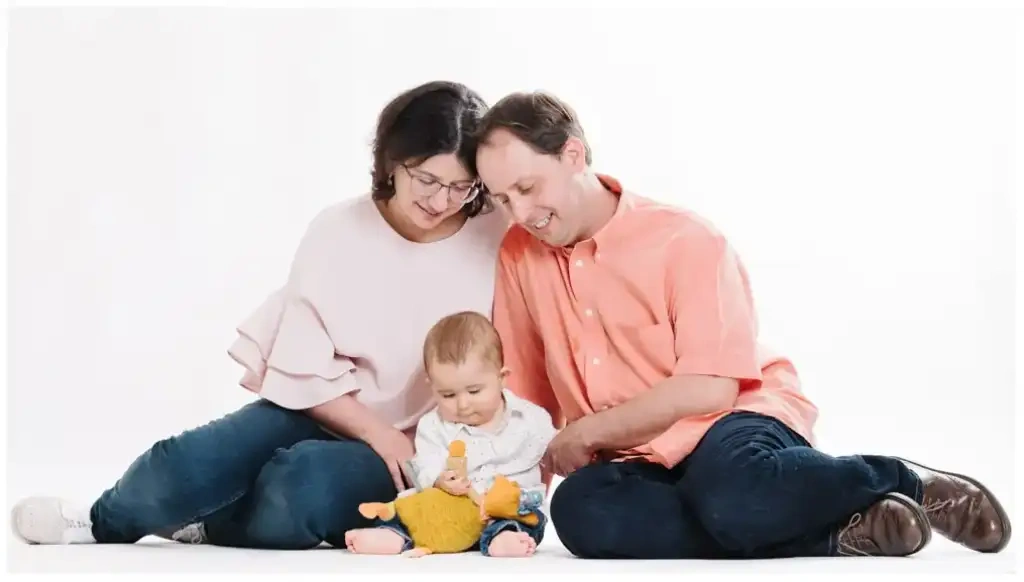 Deux parents assis au sol entourent leur bébé qui joue avec une peluche colorée.