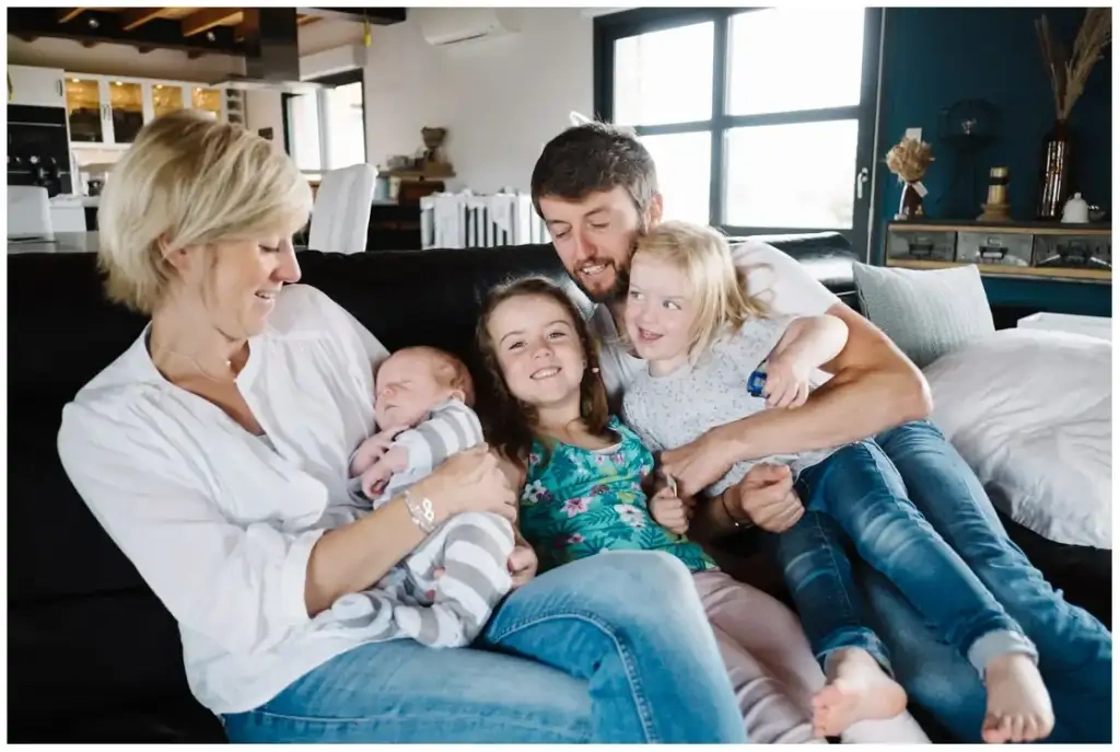 Deux parents et leurs trois enfants sont réunis sur un canapé autour du nouveau-né endormi.