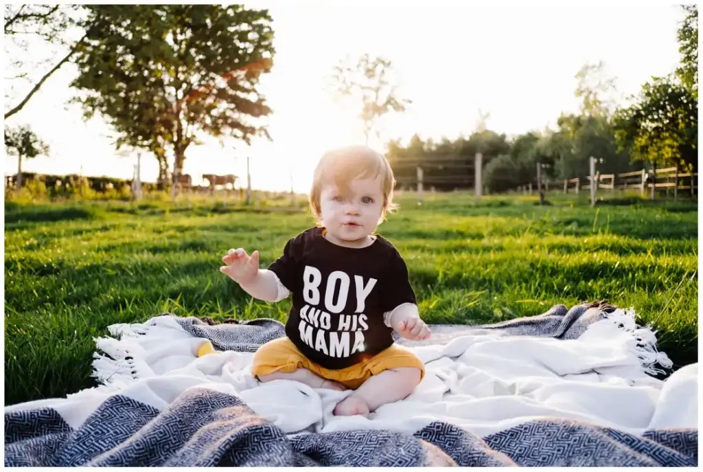 Un bébé est assis sur une couverture dans une prairie éclairée par le soleil couchant.