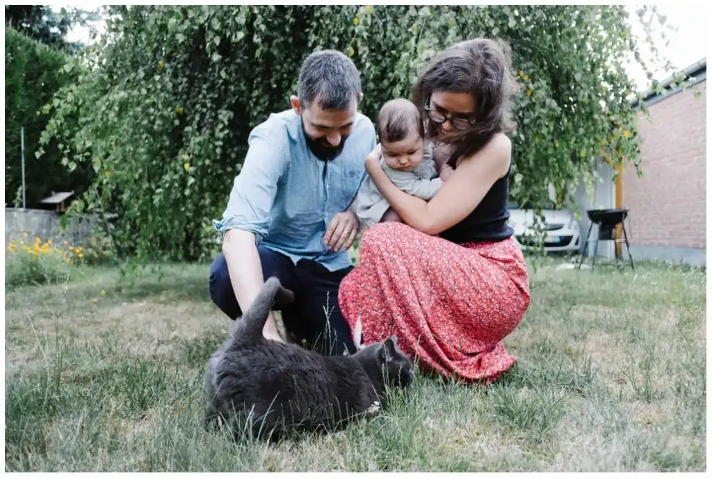 Deux parents et leur bébé observent un chat gris dans le jardin.