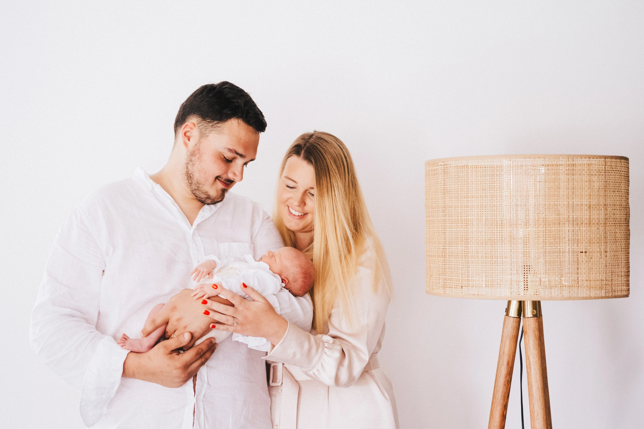 Parents souriants tenant leur nouveau-né pendant une séance photo de naissance dans un intérieur lumineux.