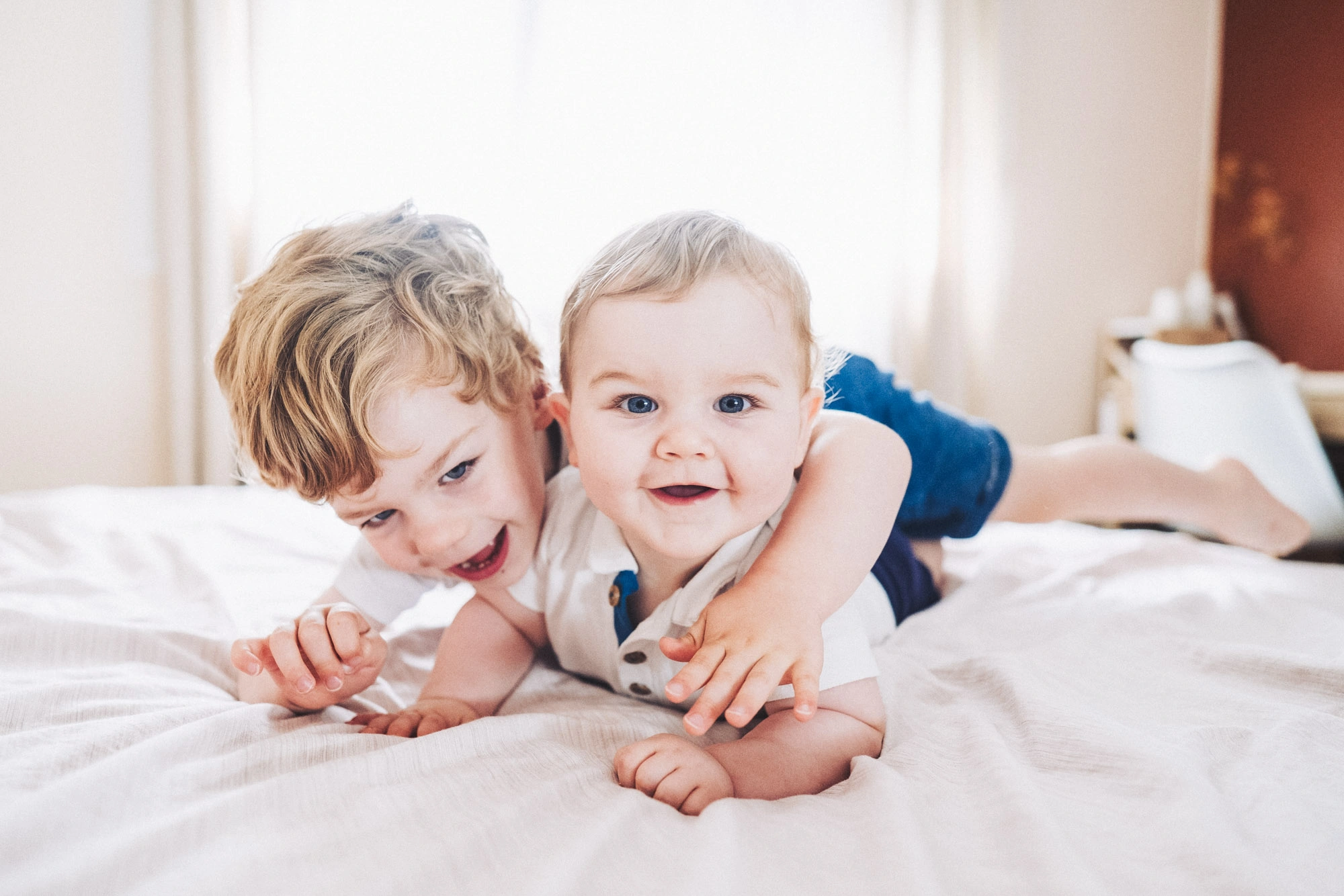 Trois enfants riant et sautant sur un lit pendant une séance photo de famille.