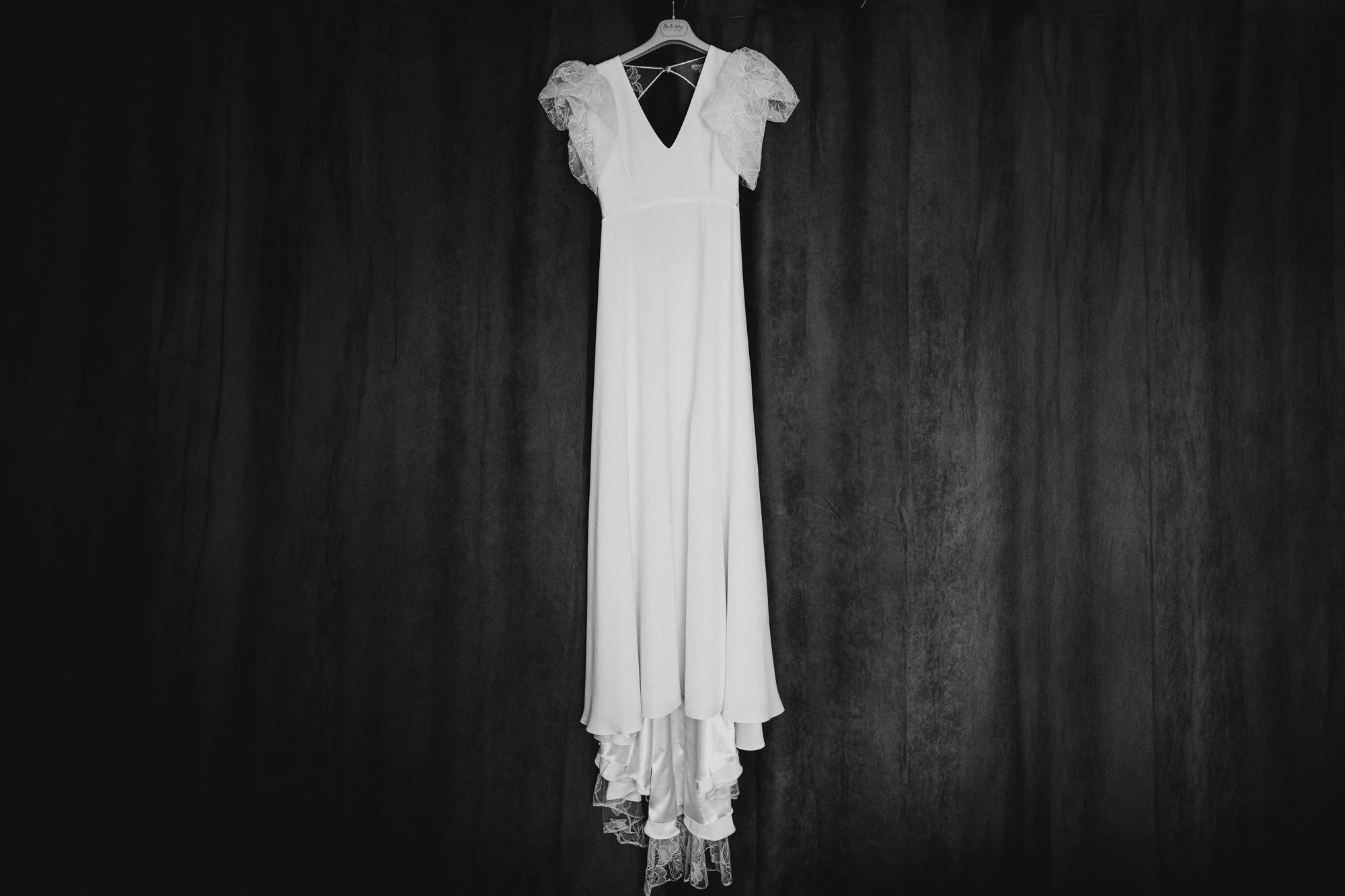 Robe de mariée blanche suspendue devant un rideau sombre en noir et blanc.