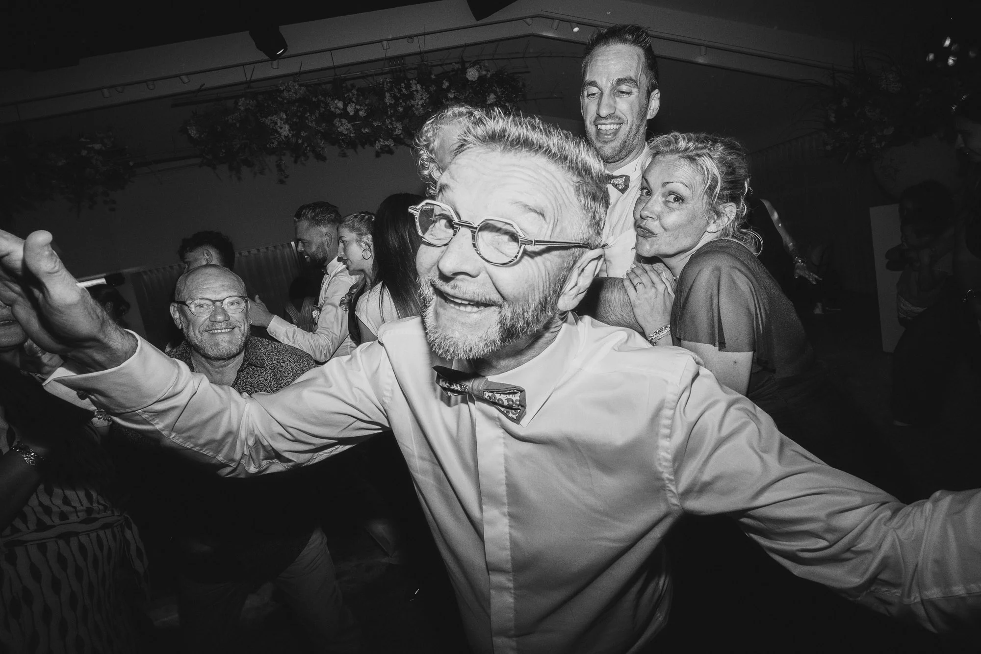 Invités réunis sur la piste de danse autour d'un homme souriant en noir et blanc.
