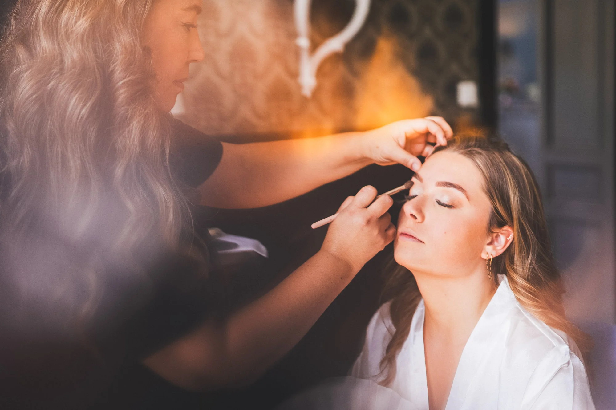 Mariée assise pendant son maquillage dans une lumière douce lors des préparatifs.