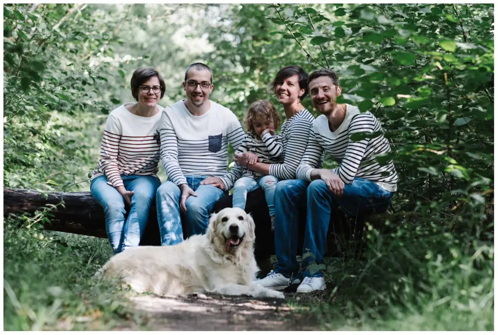 Cinq personnes assises sur un tronc en forêt avec un Golden Retriever au premier plan.