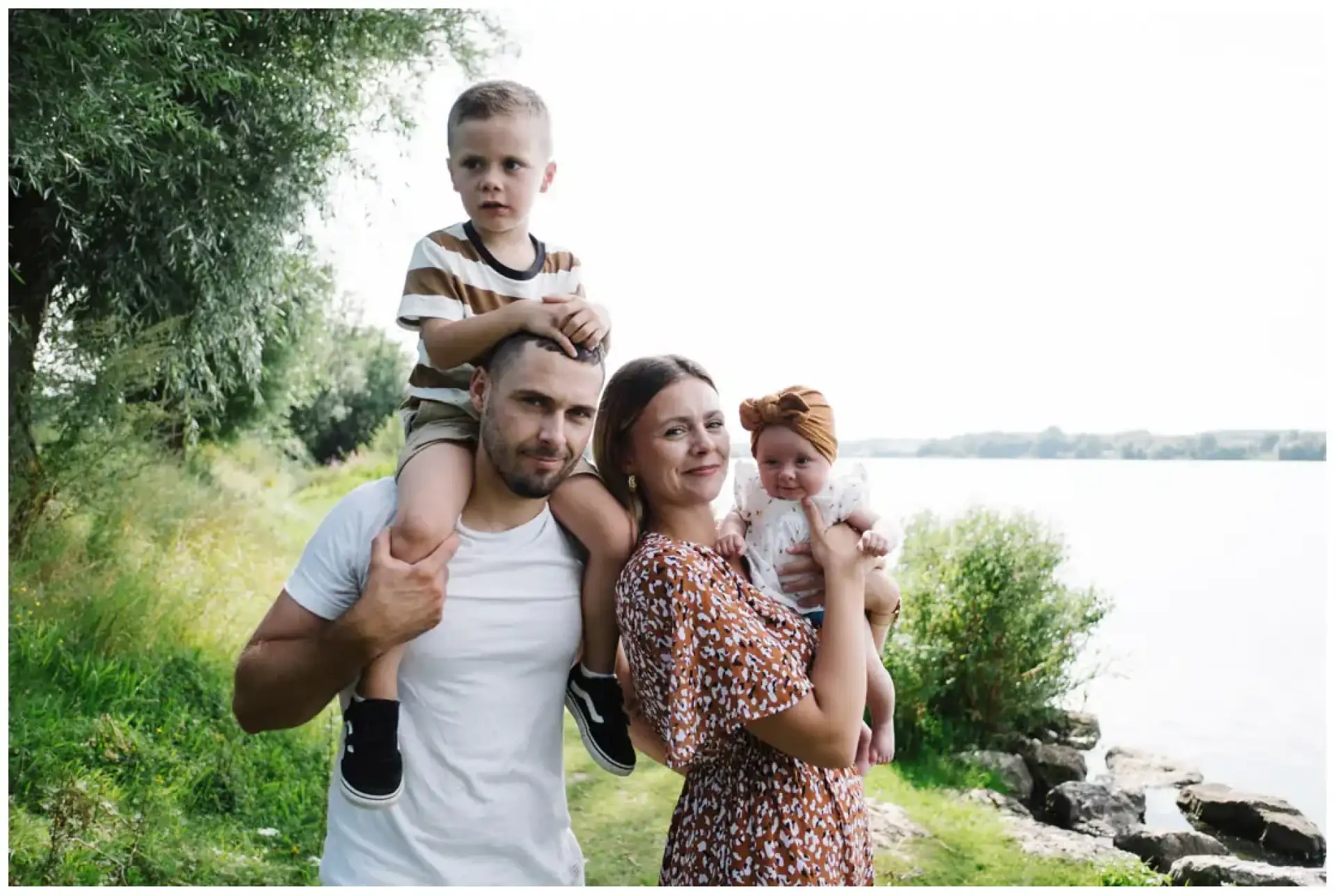 Deux parents portant leur garçon et leur bébé sur un chemin au bord d'un plan d'eau.