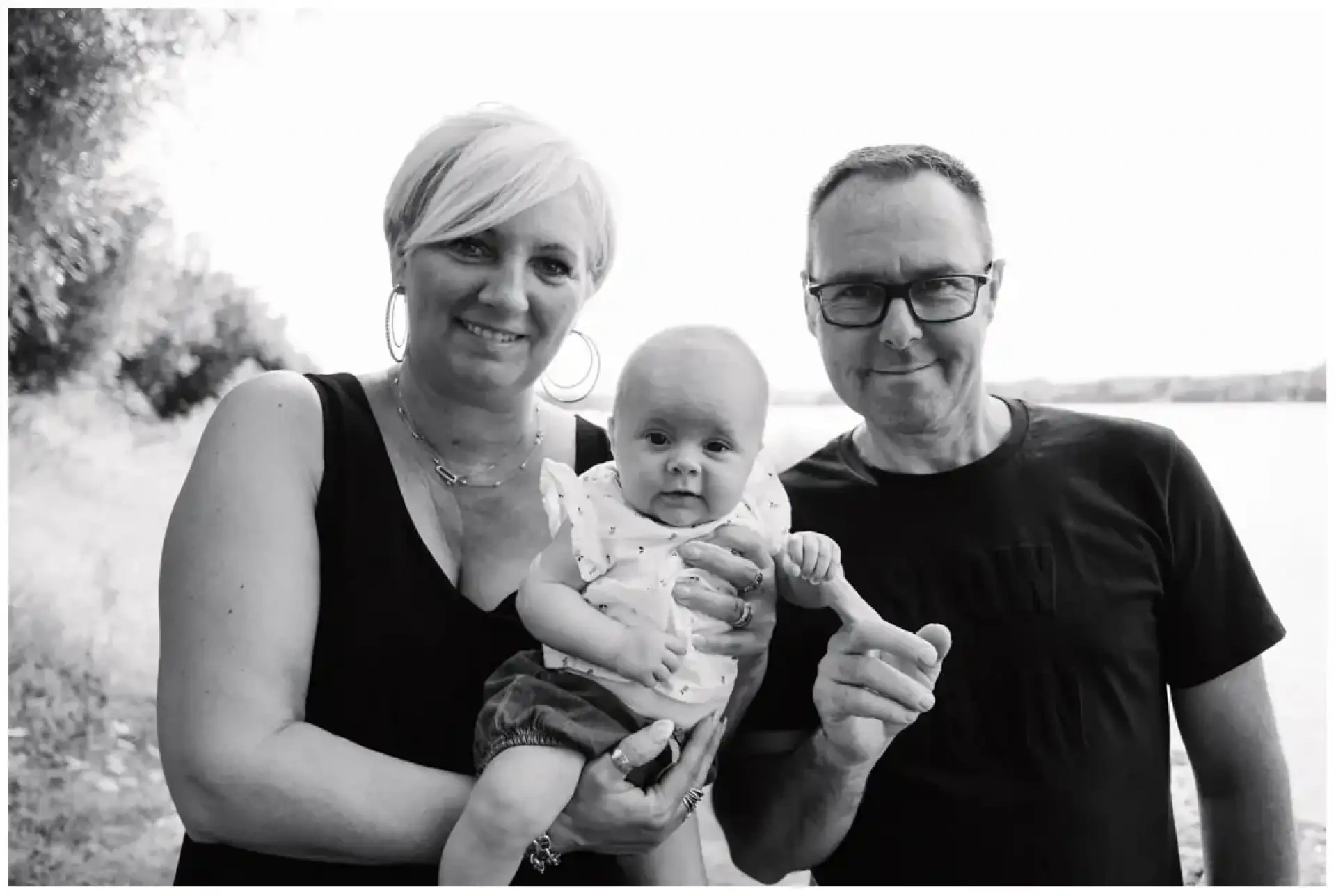 Deux adultes tenant un bébé entre eux dans un portrait en noir et blanc.