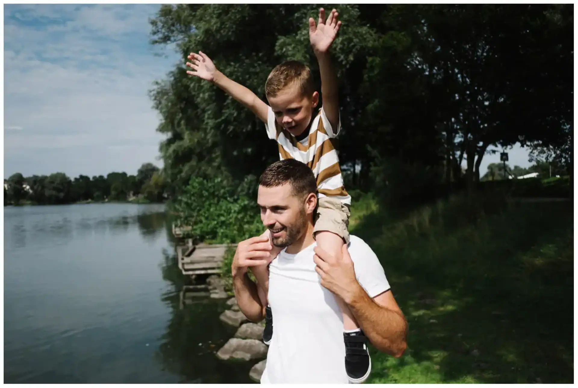 Un père portant son jeune fils sur ses épaules au bord d'un plan d'eau.