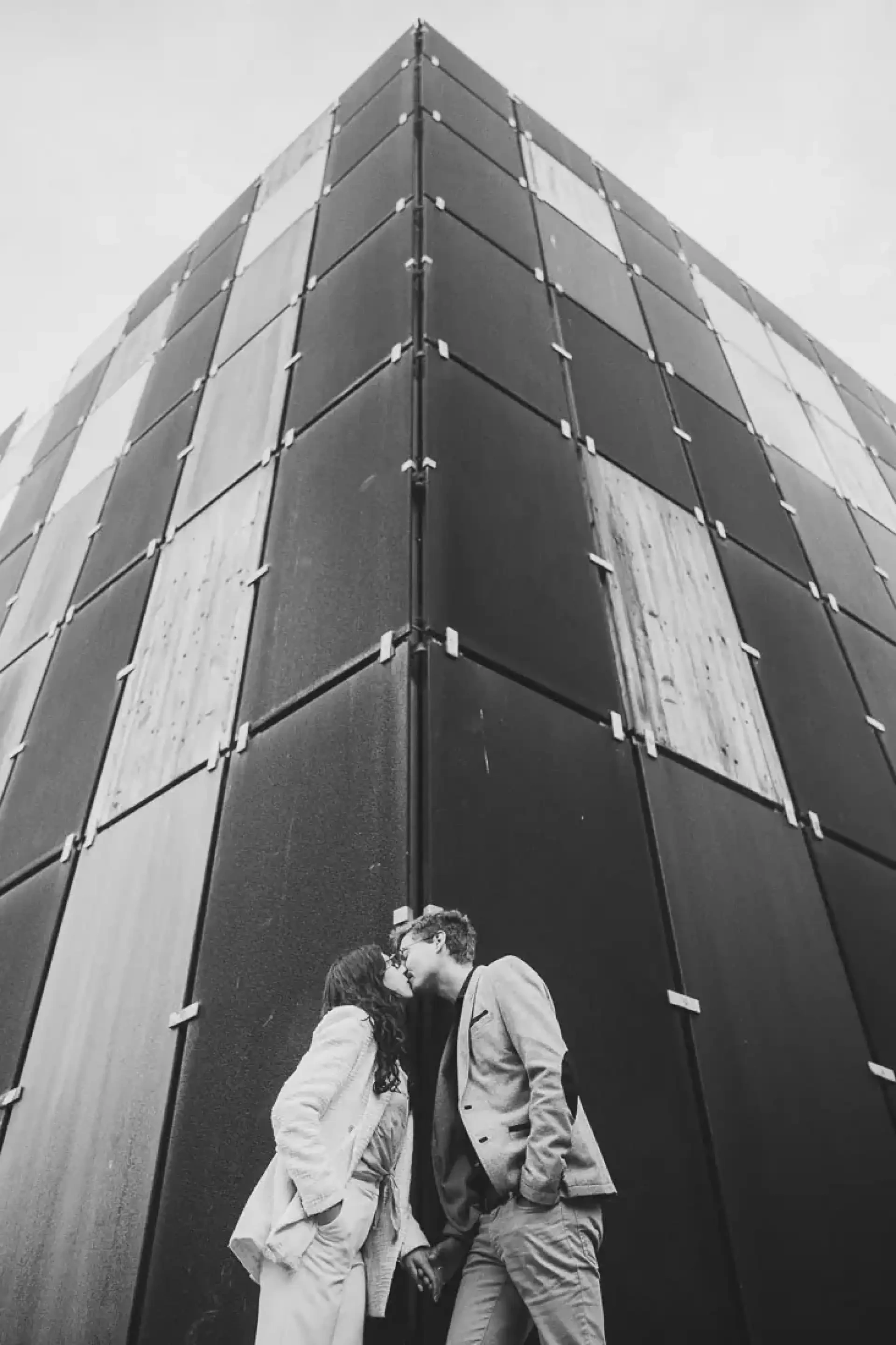 Victoire et Hubert s'embrassant au pied de la haute façade métallique du Métaphone, en noir et blanc.