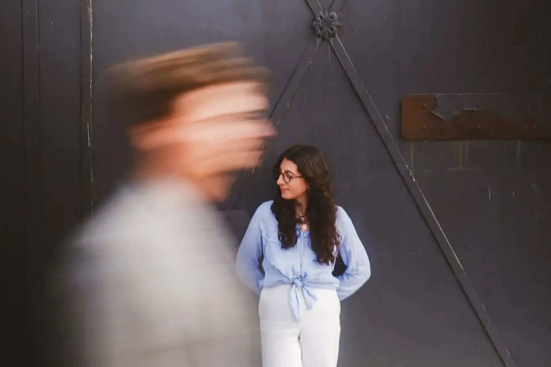 Victoire immobile devant une porte sombre tandis qu'Hubert passe devant elle dans un mouvement flou.